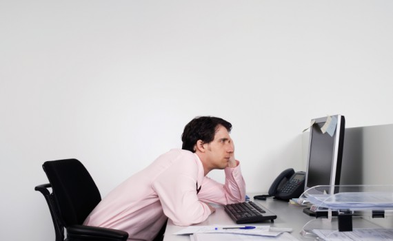 Side view of a bored male office worker looking at notes on computer monitor at desk